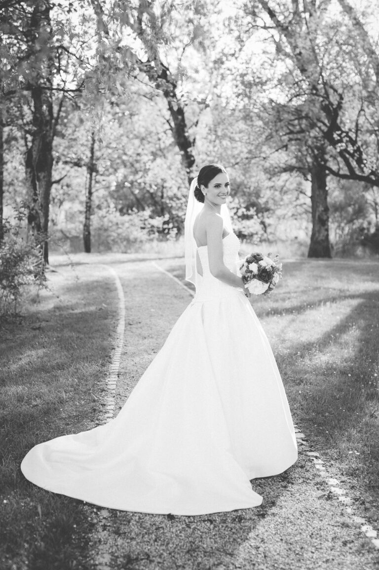 Braut in fließendem Kleid bei einem Spaziergang im Park, Schwarzweißaufnahme